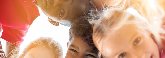 Portrait of happy kids in circle looking down and embracing. Group of five multiethnic friends outdoor looking at camera and smiling. Closeup face of smiling children looking down at the camera together at park.